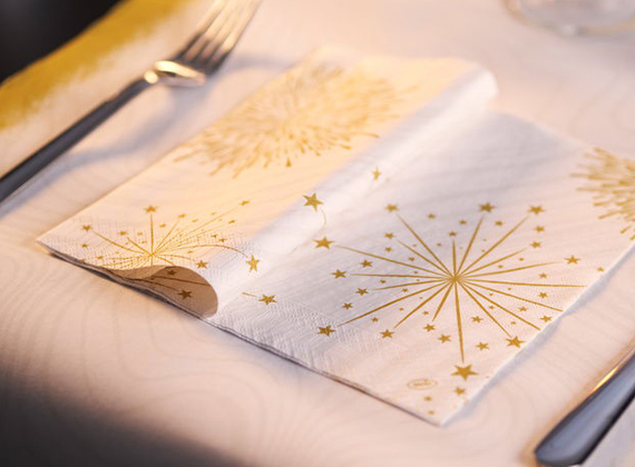 Elegant white paper napkin with gold starburst and star patterns on a festive dining table with a matching table runner.
