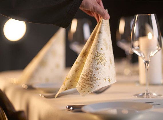 Elegant festive table setting with gold star napkin, white plates, wine glasses and candlelight – perfect for showcasing premium Christmas tableware.