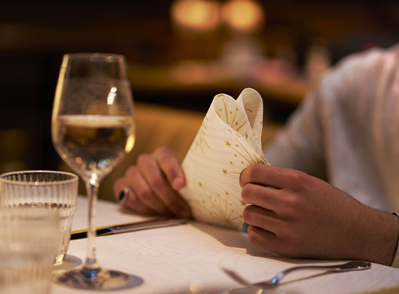 Dining table close up of a person holding a white and gold star-patterned folded napkin.