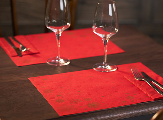 Two festive red placemats set on a bare restaurant table with wine glasses ready for service.