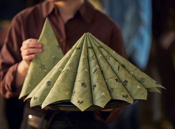 Festive pistachio green napkin folded into a Christmas tree shape with seasonal motifs – a trendy and elegant touch for holiday table settings.